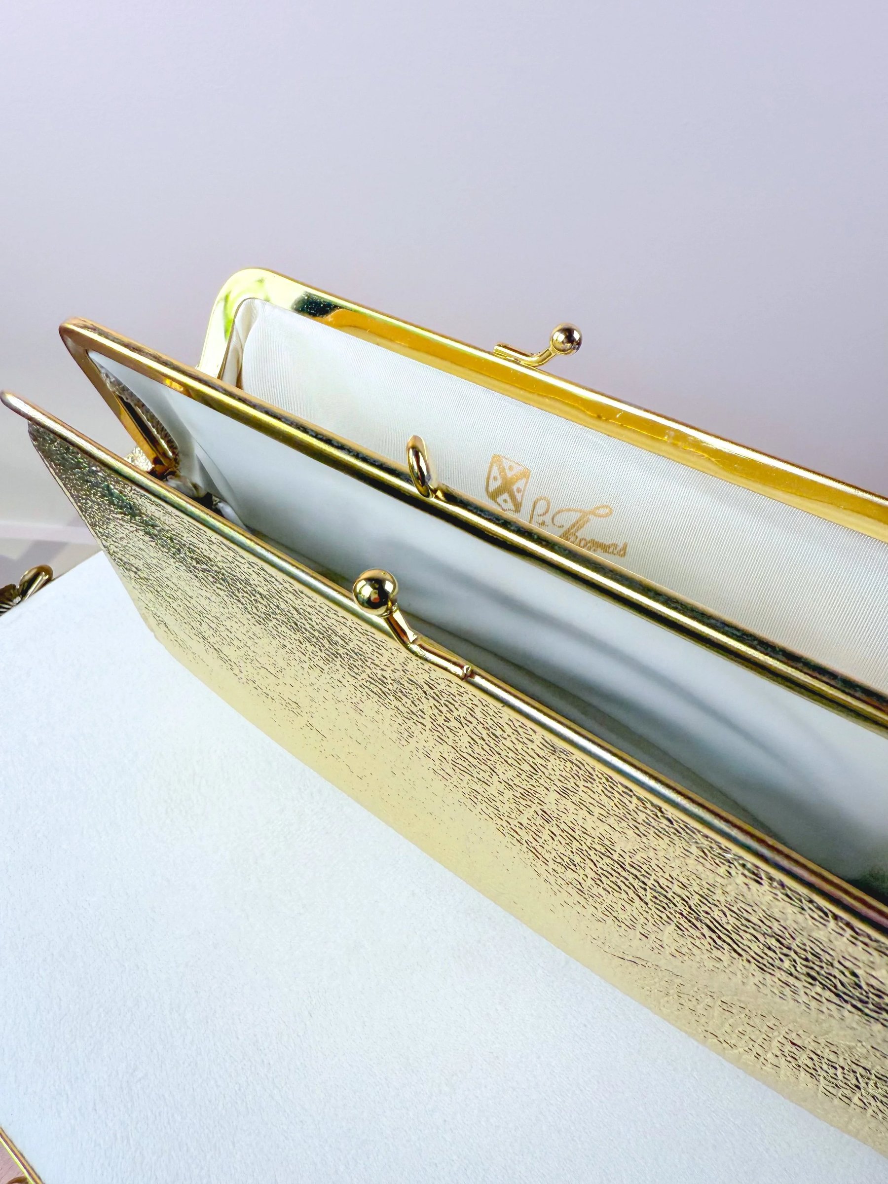 A gold metallic handbag with a textured finish and a clasp closure, featuring a white interior.