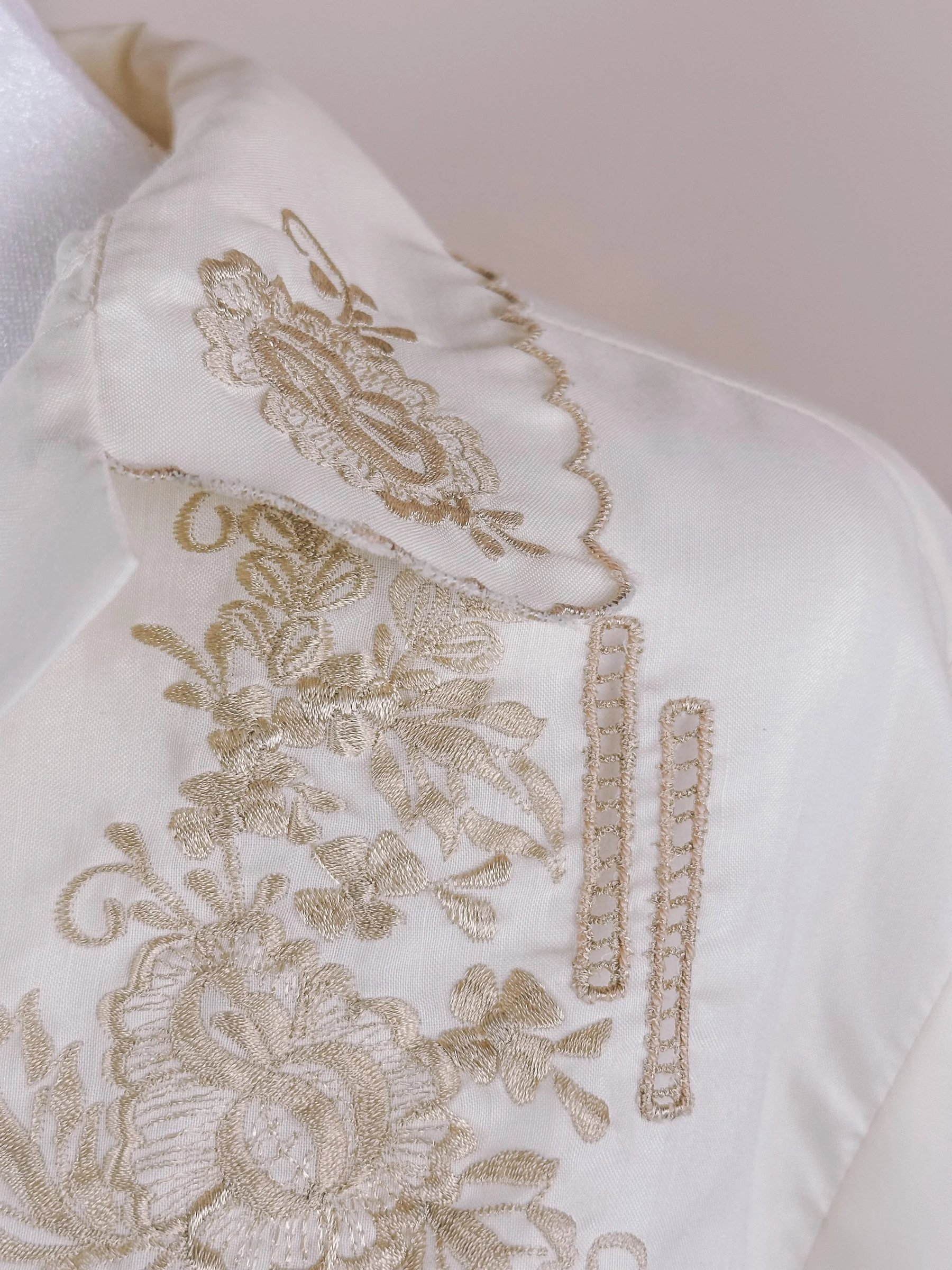 White fabric featuring intricate gold embroidery on the collar and front panel.