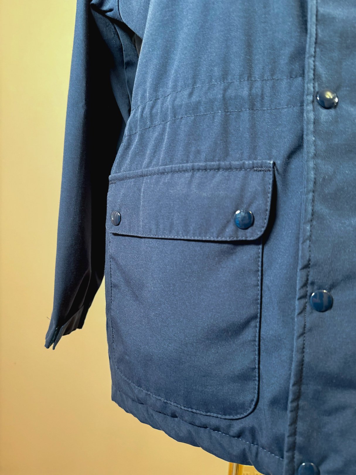 Navy blue women's utility field coat from the 1970s featuring a large front pocket and snap closures.