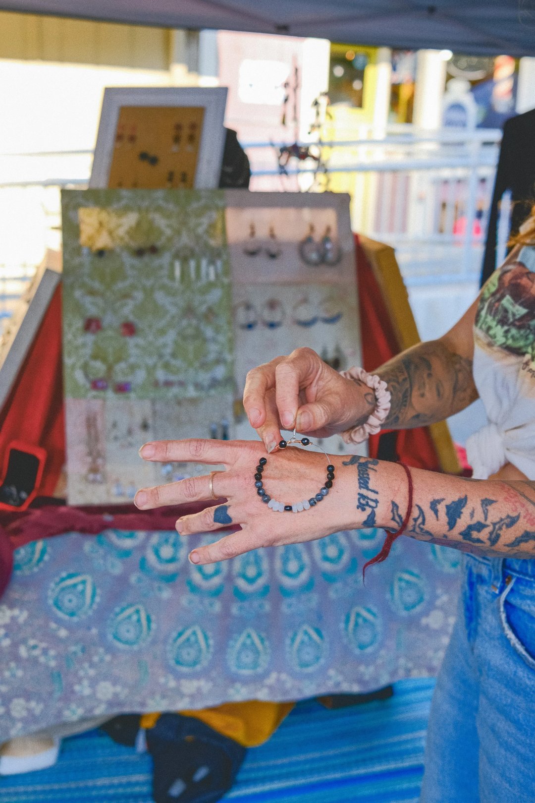 A person displaying a beaded bracelet on their wrist in front of a jewelry display at an outdoor market.
