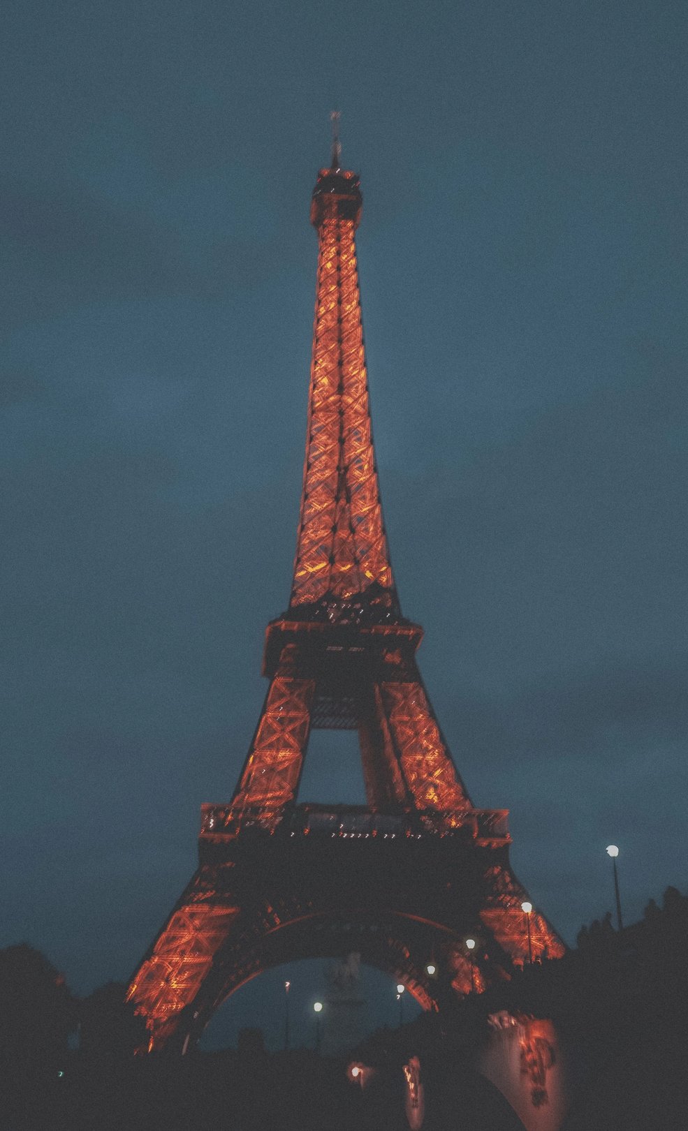 The Eiffel Tower illuminated in orange against a dark night sky.