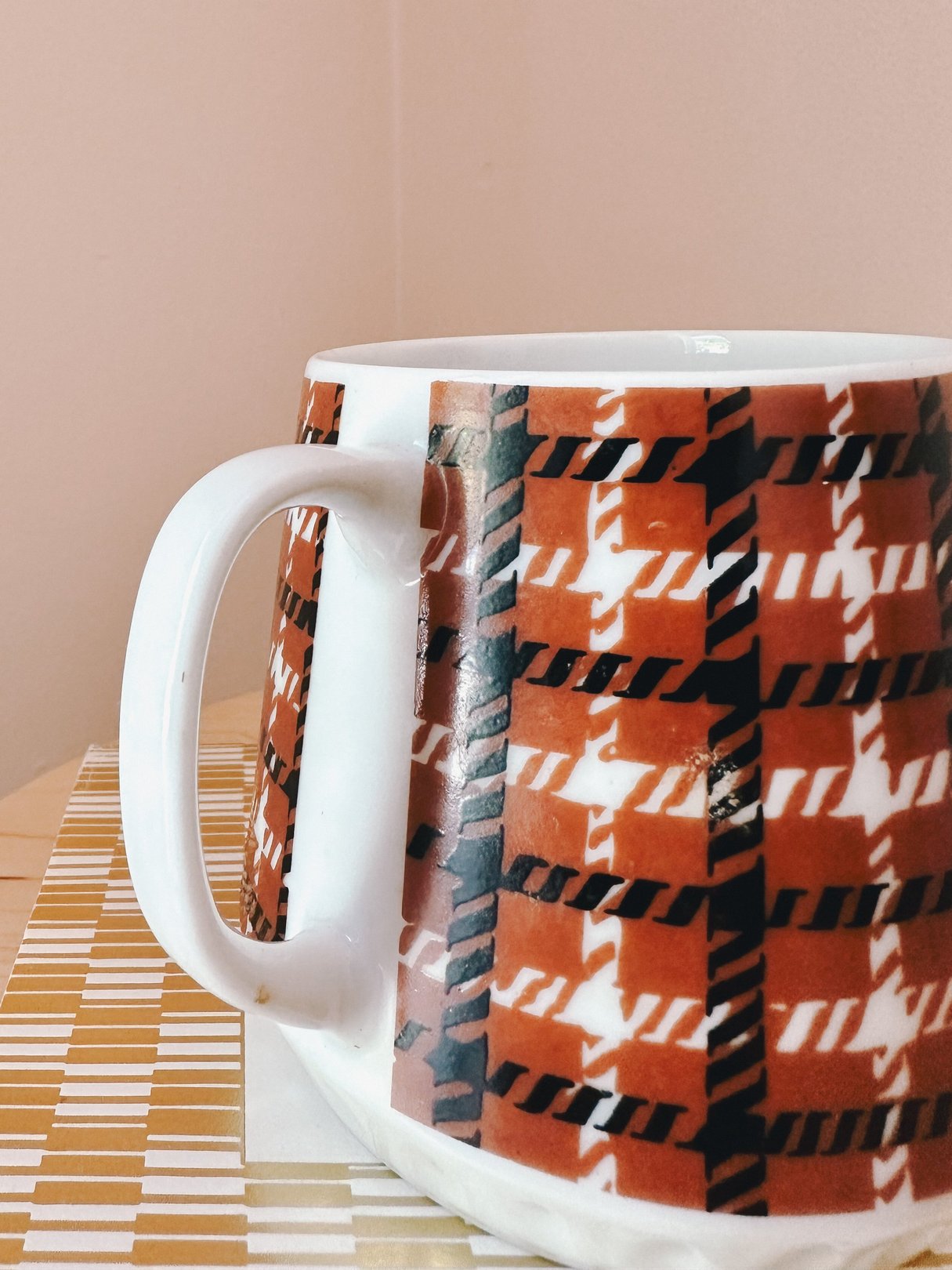 A 1970s houndstooth print mug in black and red with a white handle, suitable for home decor.