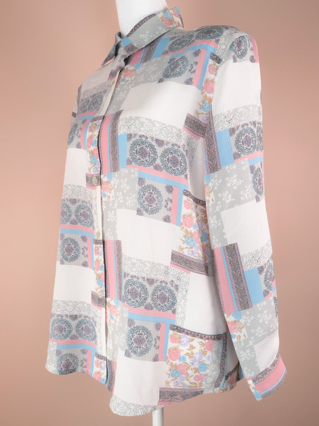 A 1980s women’s blouse featuring a patchwork design with floral and geometric patterns in white, pink, grey, and blue.