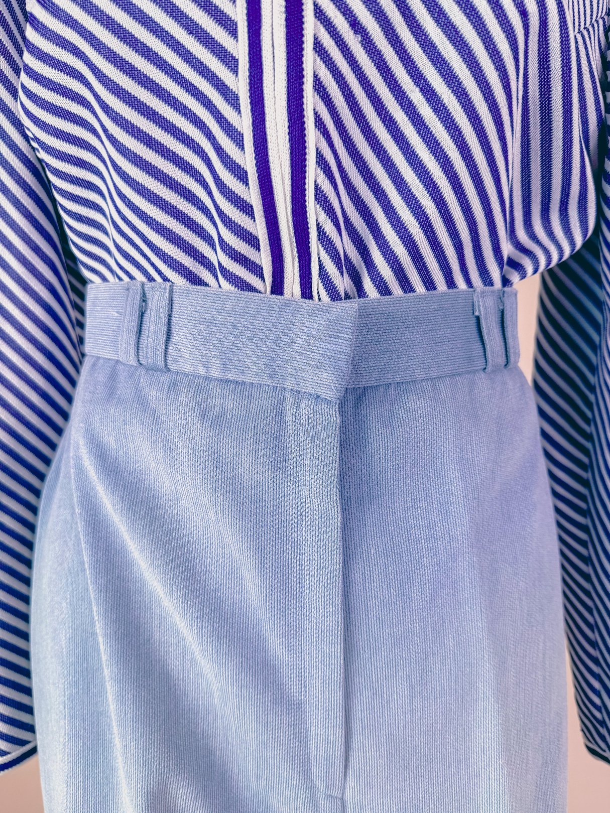 Light blue high-waisted pants featuring a pleated front, suitable for women and inspired by 1970s fashion.