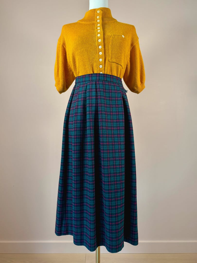 A 1970s women's rolling hills plaid skirt in green, styled with a mustard yellow button-up top.