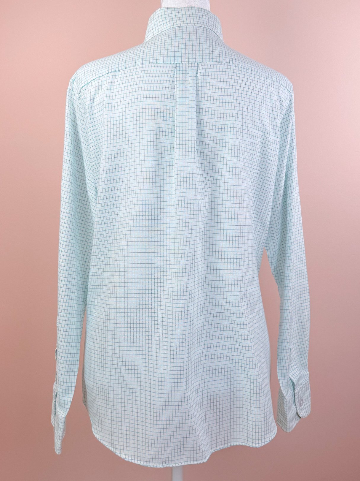Women's 1980s preppy checkered button-down shirt in white, featuring a classic collar and long sleeves, displayed on a mannequin against a pink background.