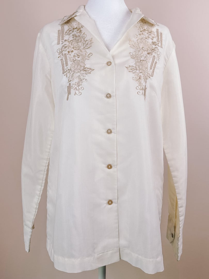 Cream-colored hand-embroidered blouse with scalloped edges and button-down front, featuring floral designs and long sleeves, from the 1950s for women.