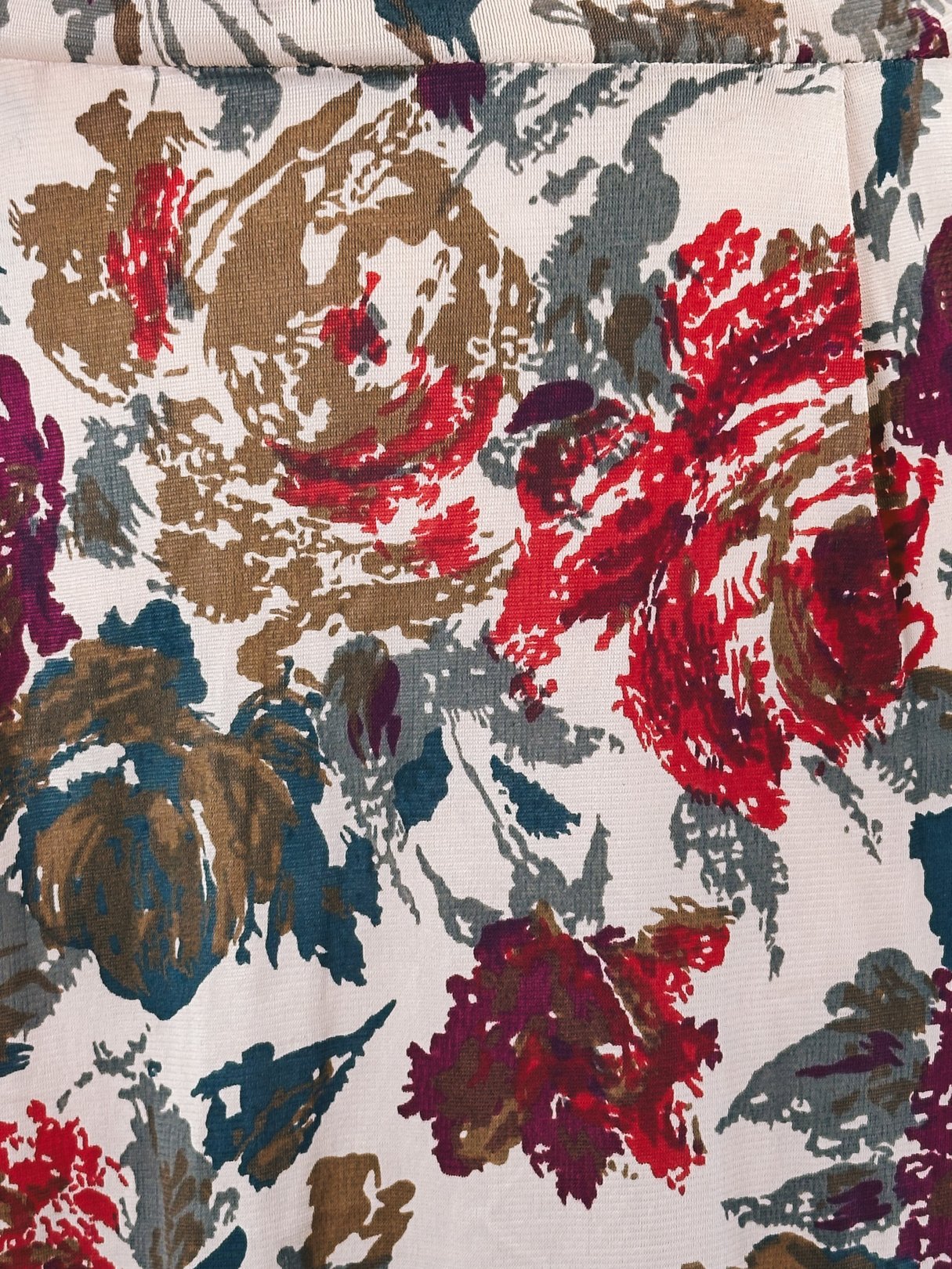A close-up of a red floral fabric featuring roses in shades of red, brown, and teal, typical of the 1960s style used in women's dresses.