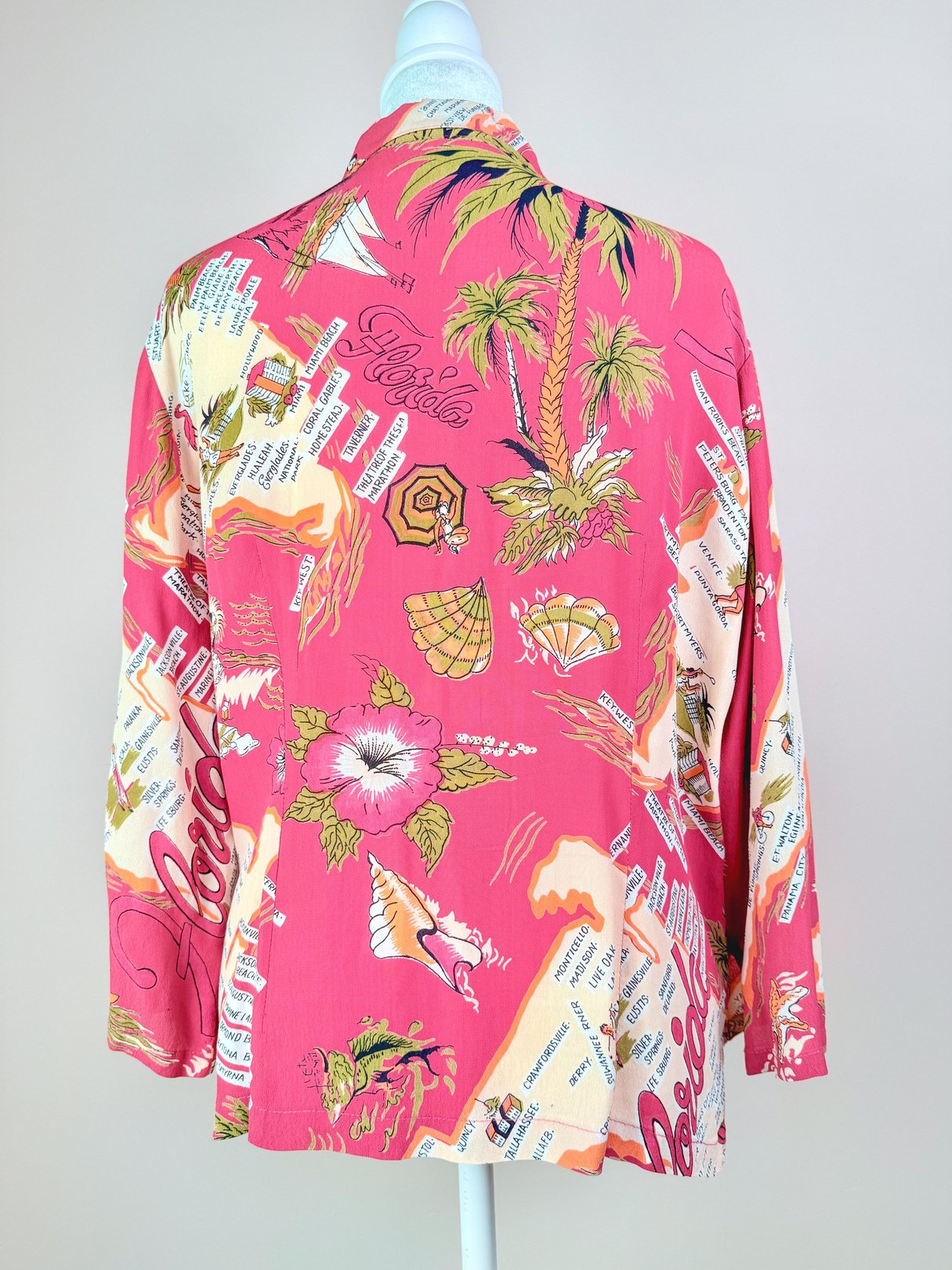 A vintage women's top from the 1970s in white featuring colorful graphics of palm trees, seashells, and tropical motifs.