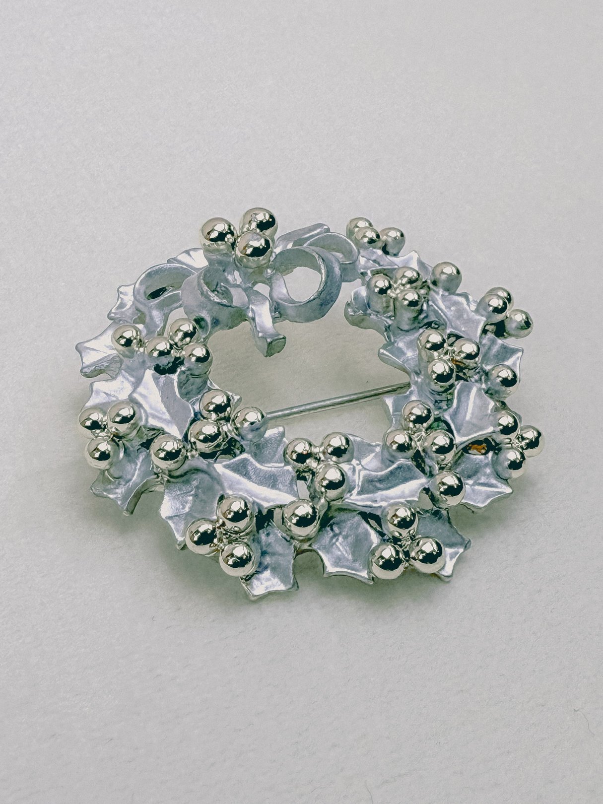 Silver 1970s keepsake wreath brooch featuring holly leaves and decorative berries.