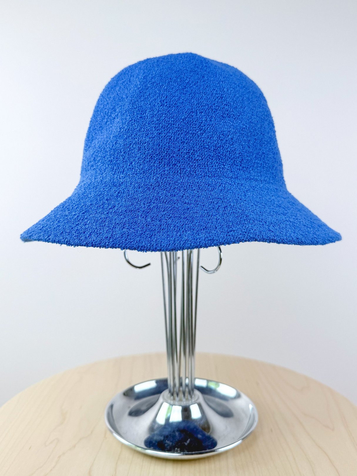 A textured cobalt blue bucket hat displayed on a metal stand.