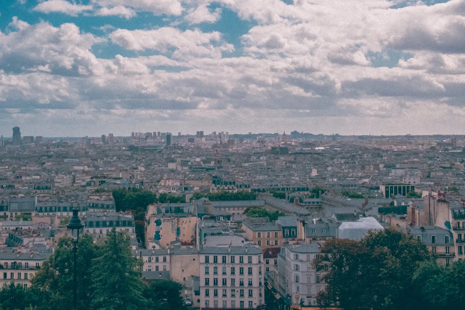 A panoramic view of Paris featuring rooftops, buildings, and a cloudy sky.