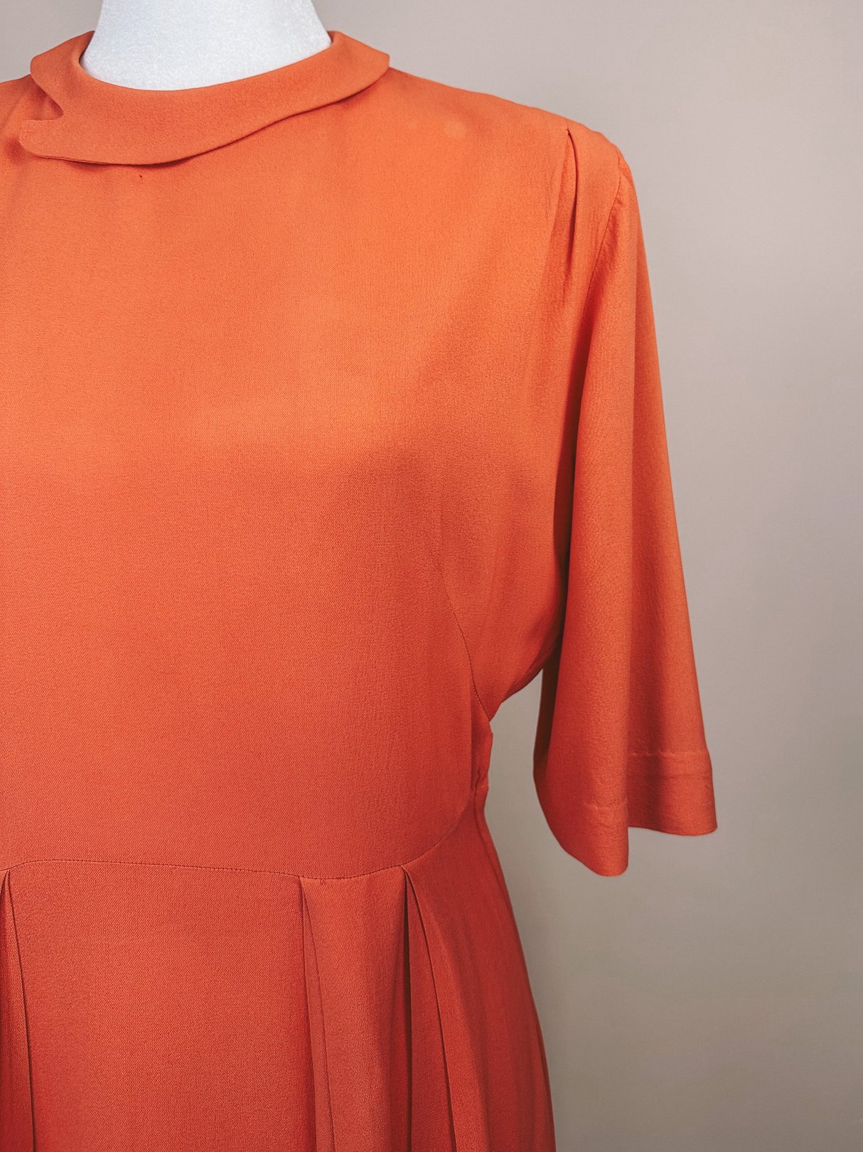 1940s coral dress featuring a high neckline, short sleeves, and a pleated skirt.