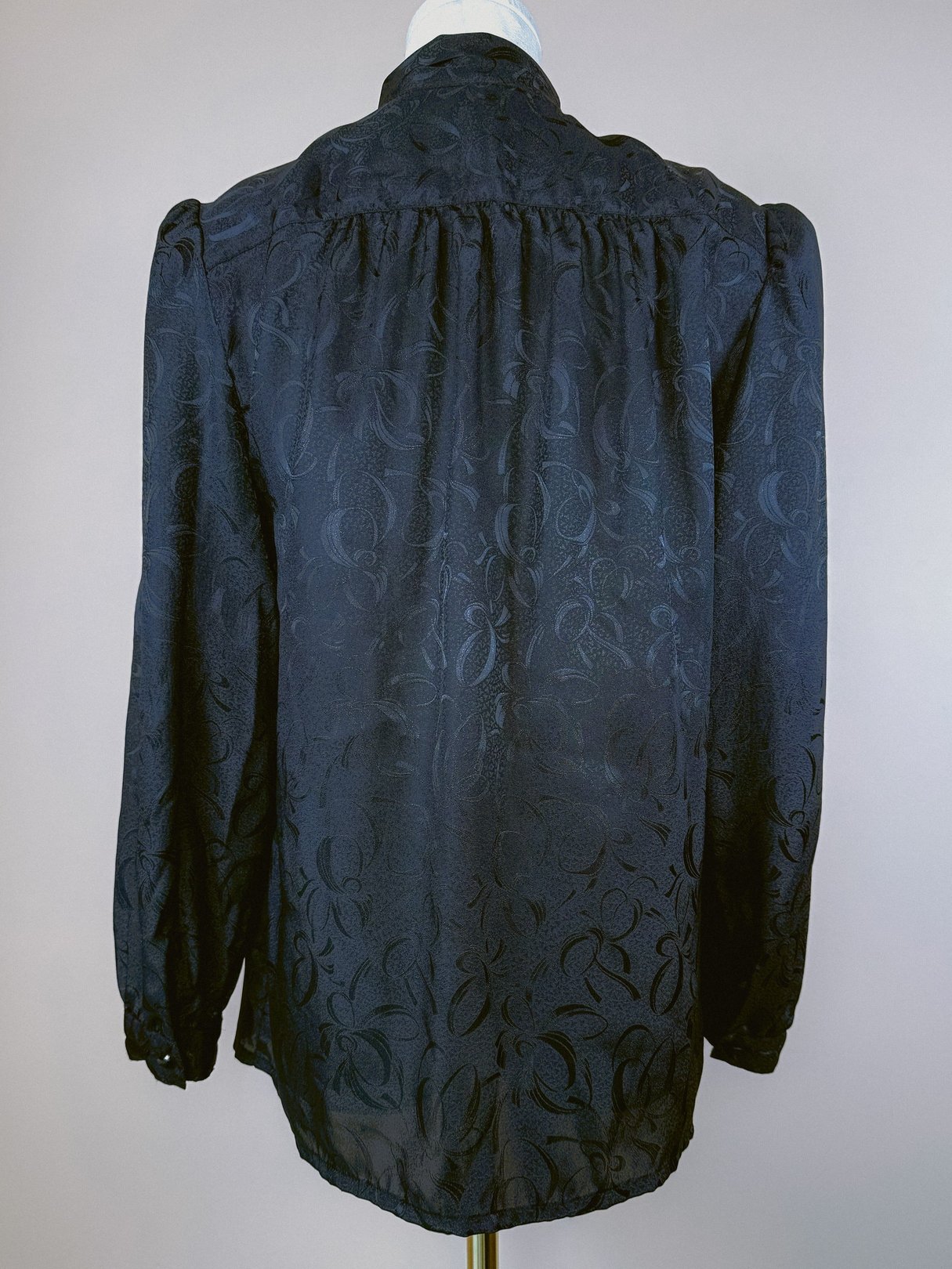 Black 1980s women's top with a bow tie detail and floral pattern, featuring long sleeves and a structured silhouette.