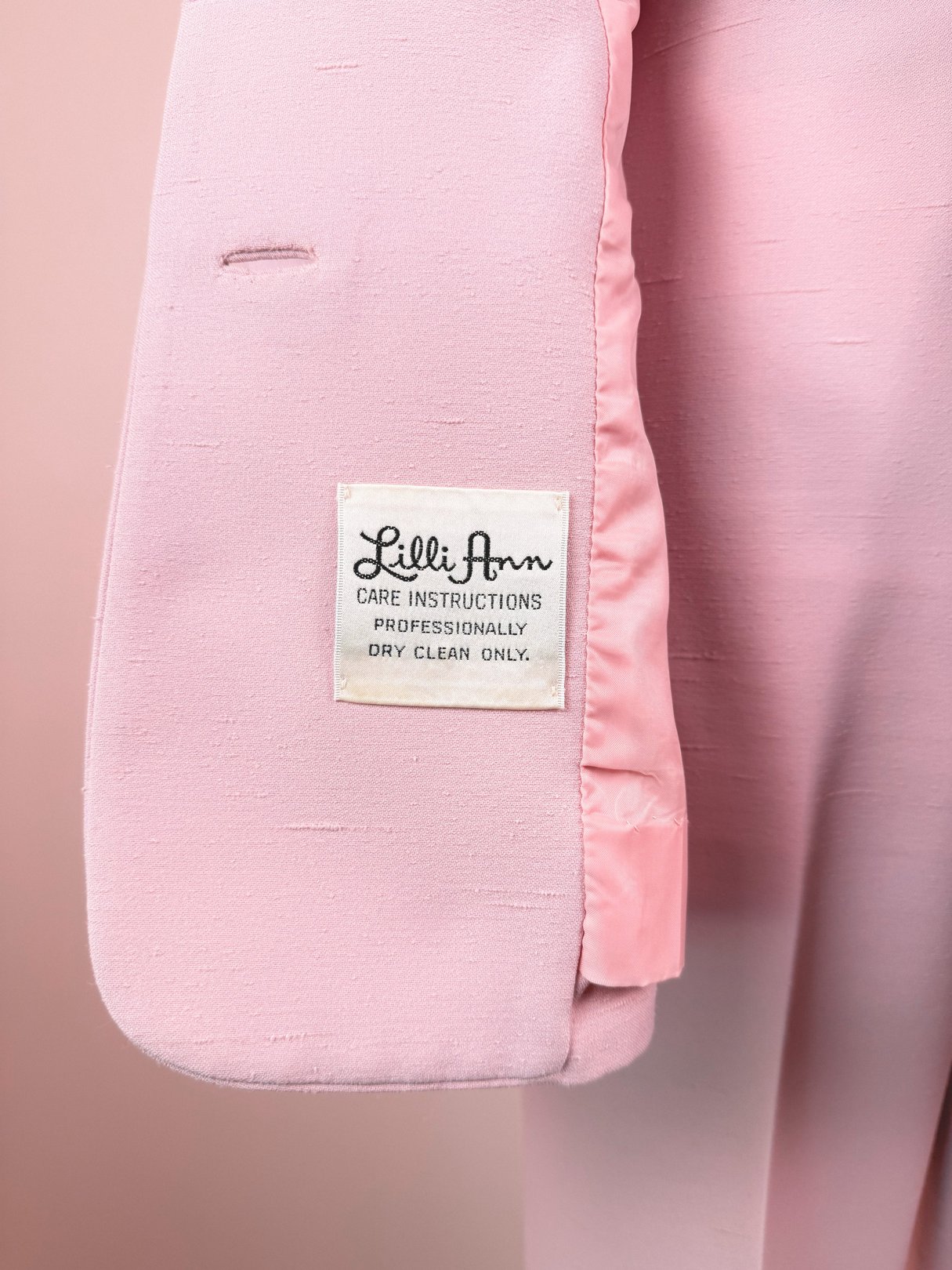 Blush pink tag with "Lilli Ann" label and care instructions, part of a 1970s women's three-piece skirt suit.