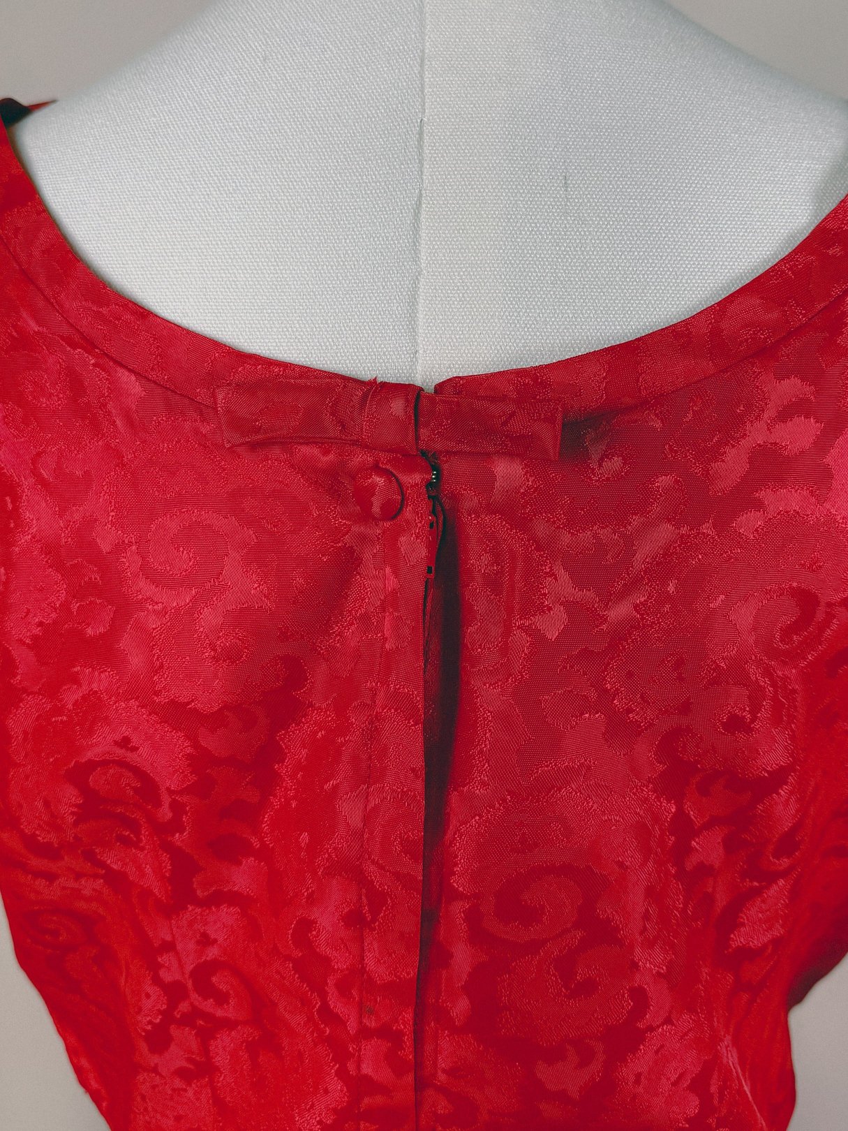Back view of a 1950s women’s red damask dress featuring a zip closure and intricate fabric texture.