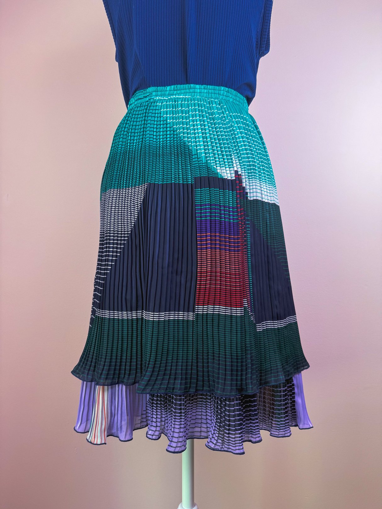 Green pleated skirt with a colorful abstract pattern, featuring a layered hem, designed for women and inspired by 1970s fashion.