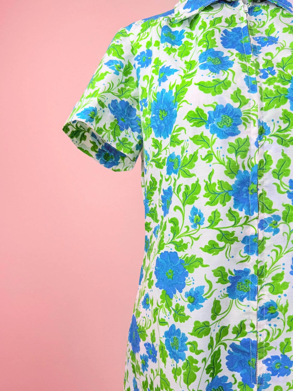A short-sleeved dress featuring a vibrant floral pattern in blue and green against a pink background.