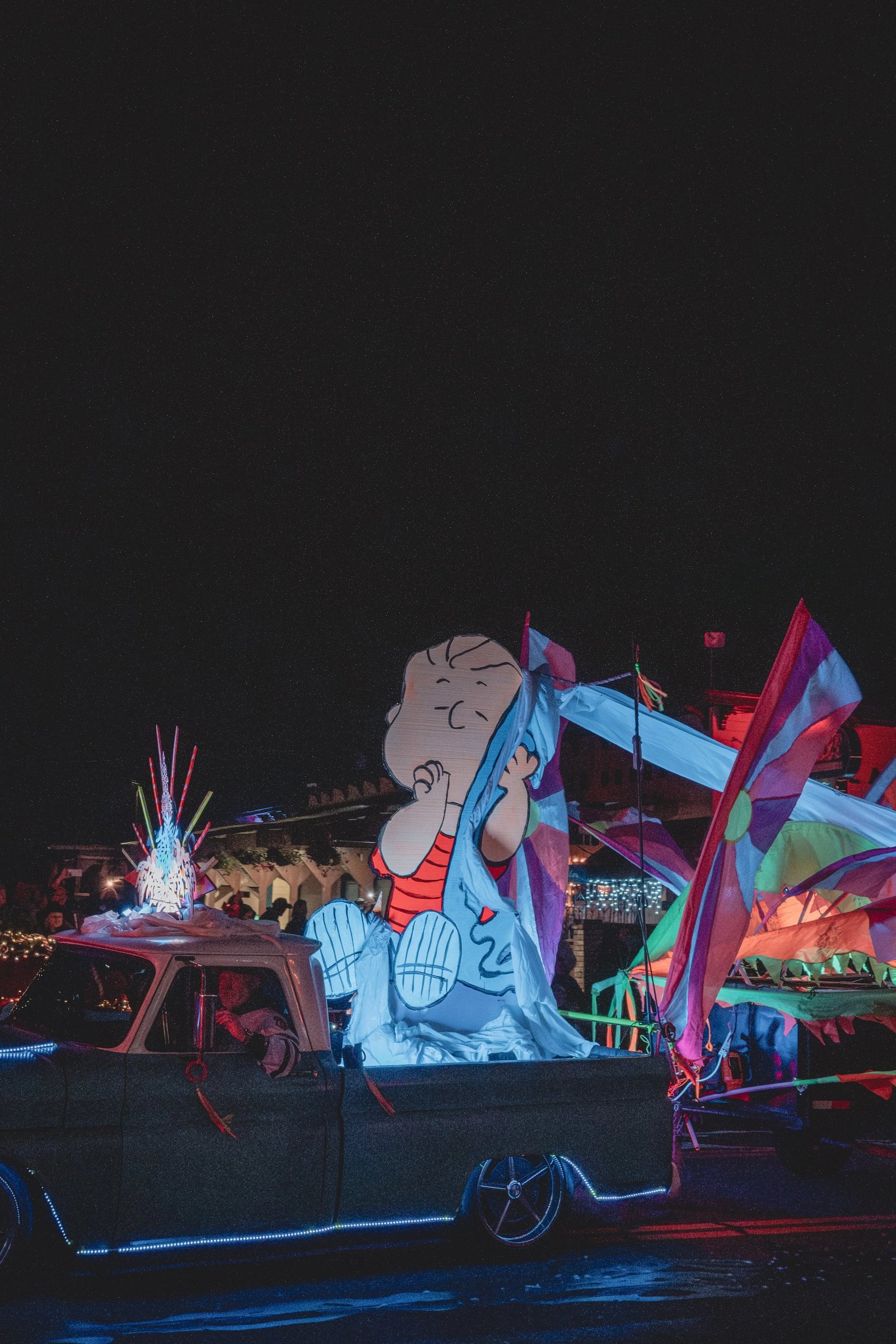 A large, colorful inflatable decoration of a cartoon character is displayed on a vehicle at a nighttime event.