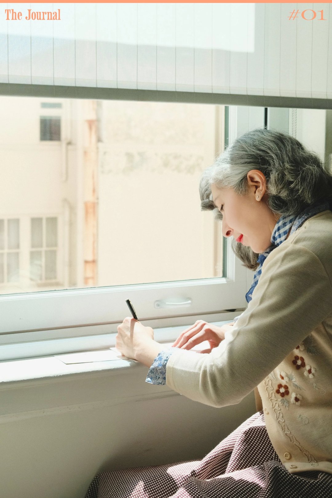 A woman with gray hair writes on a notepad while sitting by a window.