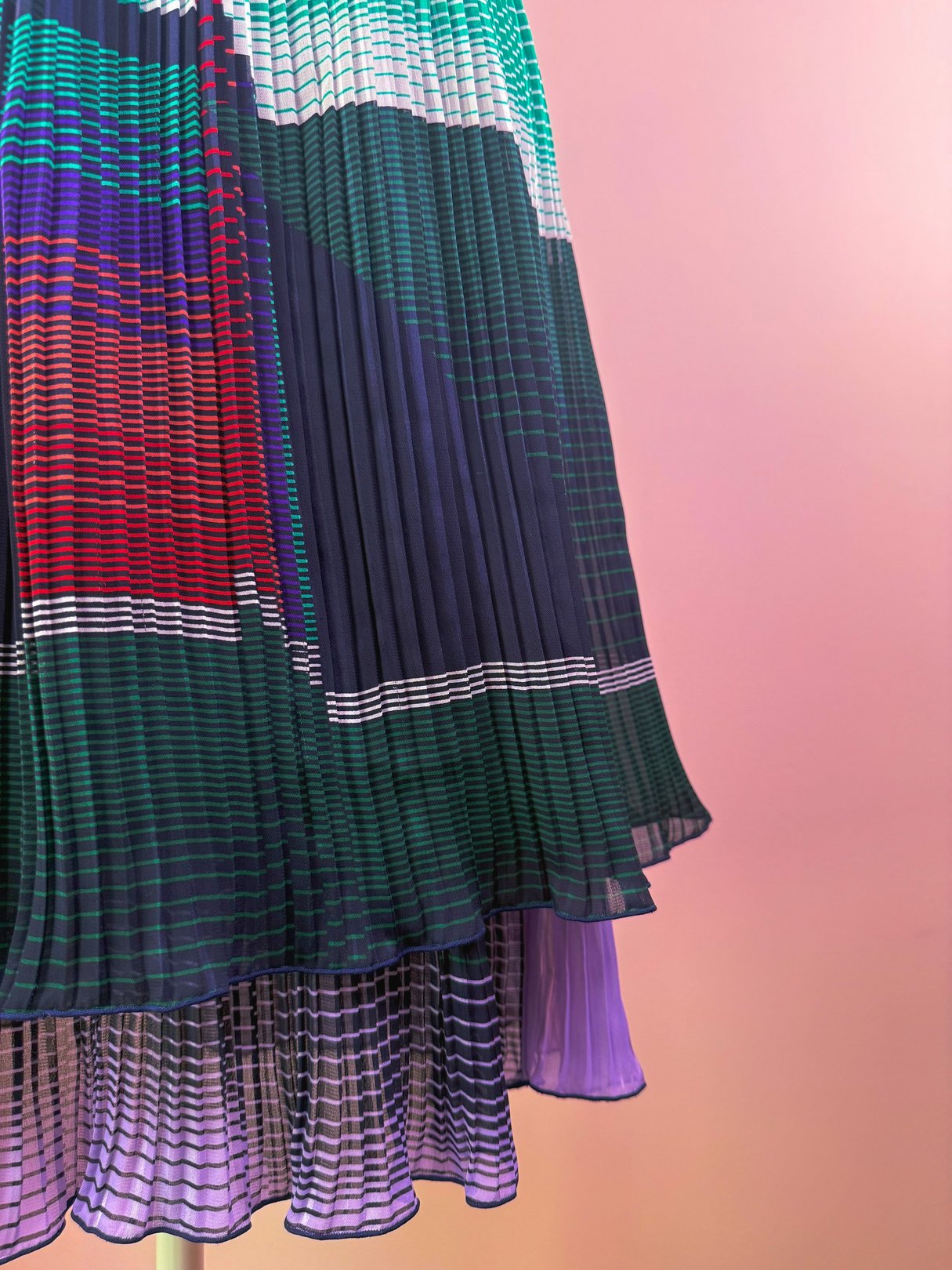A green 1970s-style pleated skirt featuring multicolored stripes and a flowing bottom hem.