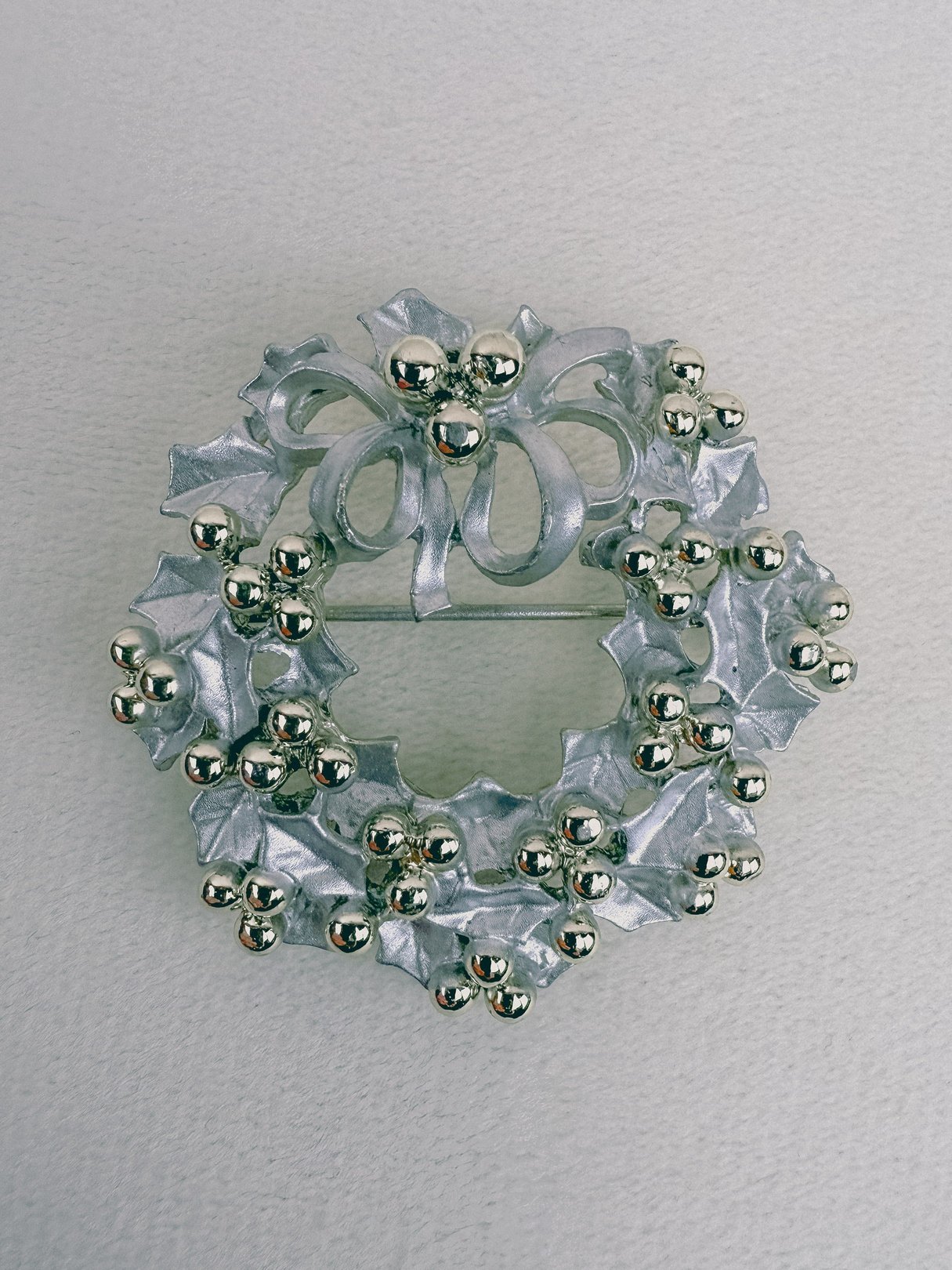 A 1970s silver wreath brooch featuring holly leaves and berries with a bow at the top.