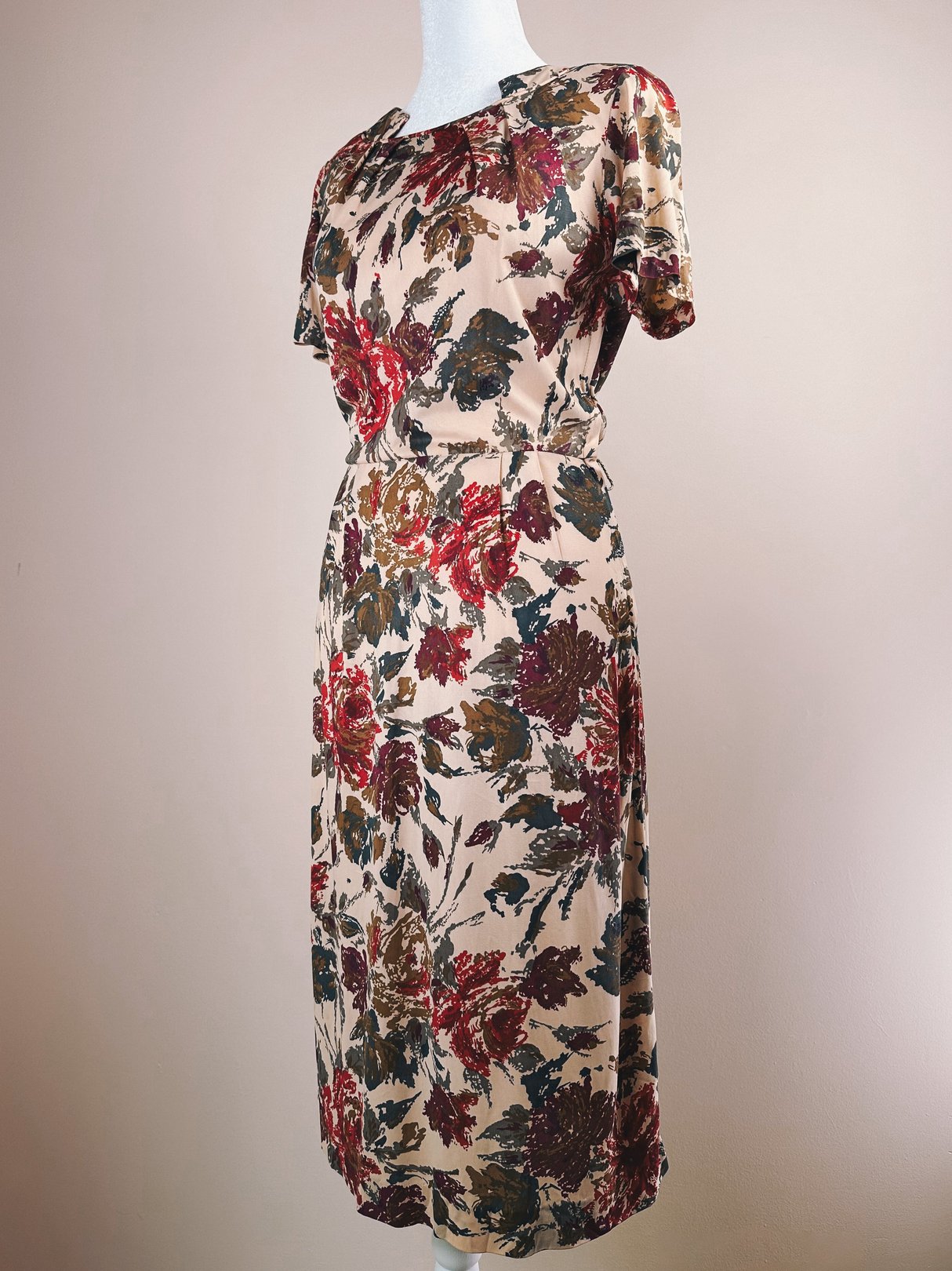 A 1960s women’s dress featuring a rose floral pattern in red, beige, and green colors with a fitted waist and short sleeves.