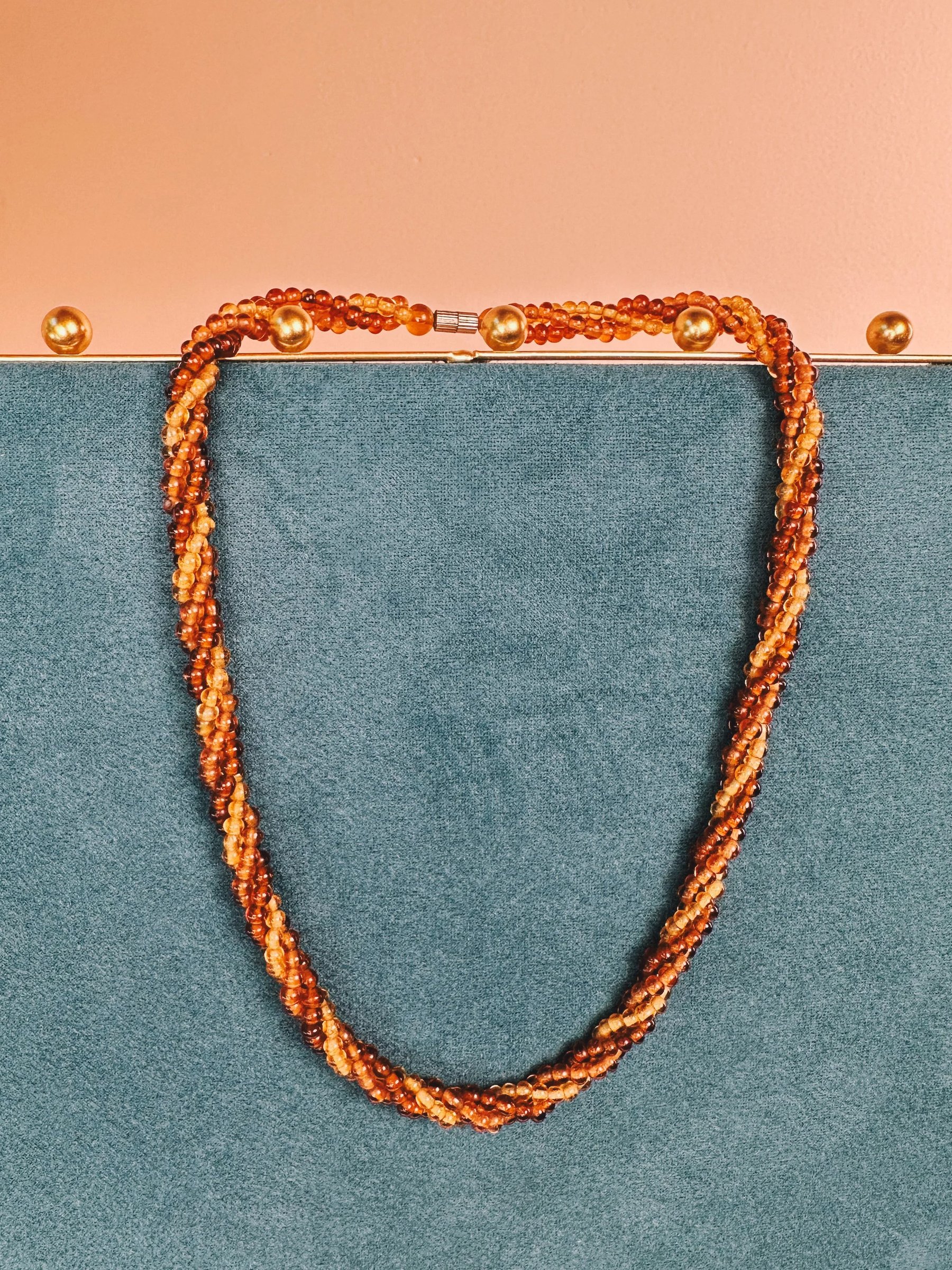 A twisted copper necklace displayed against a teal background.