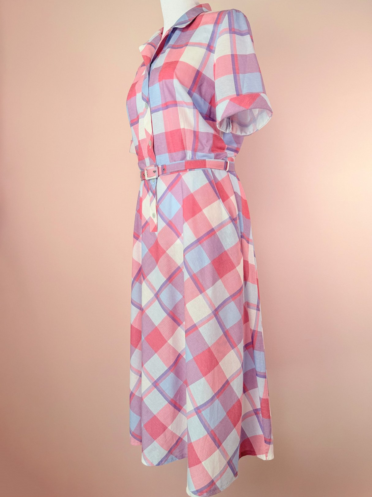 A 1950s women's dress featuring a purple and pink plaid pattern, short sleeves, a buttoned front, and a matching belt.