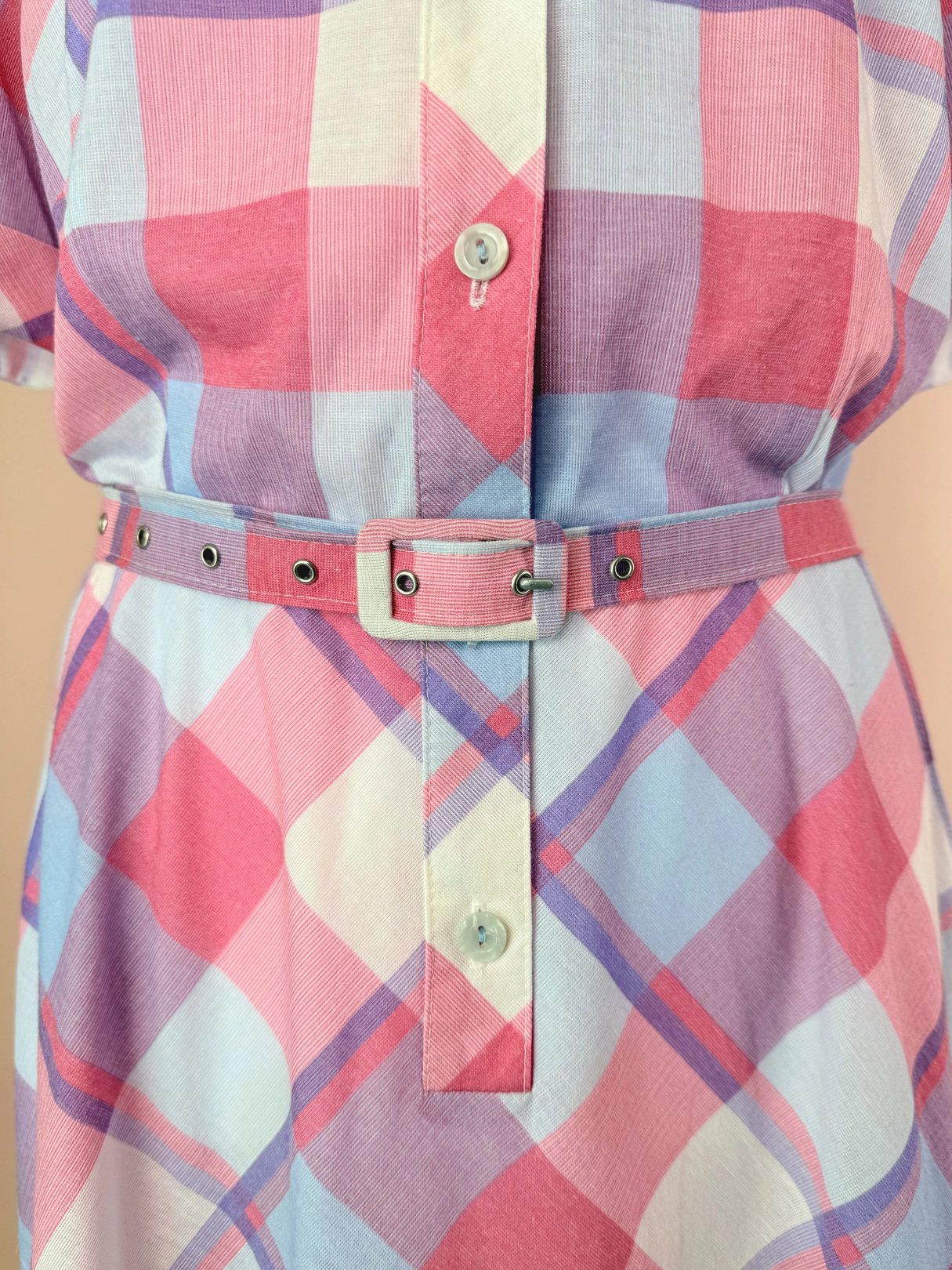 A close-up of a plaid shirt in pink and light blue tones featuring a belted waist.