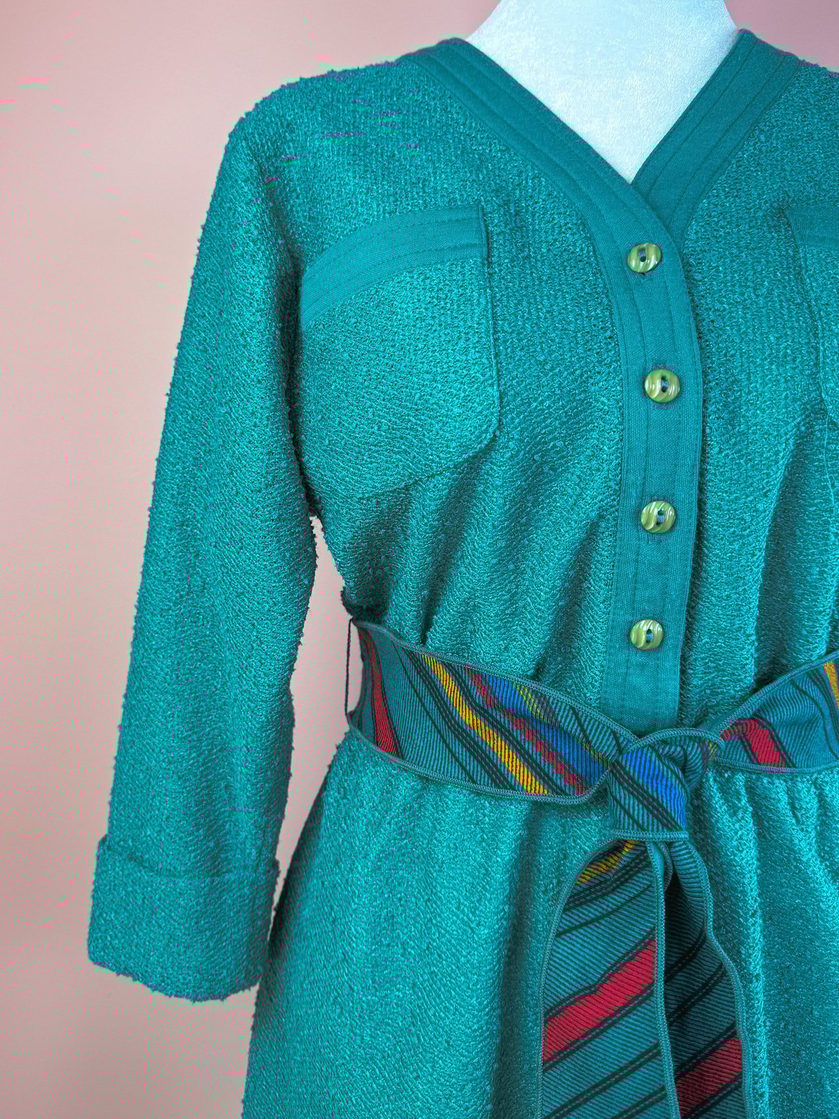 Teal 1980s women's dress featuring a textured fabric, button front, two chest pockets, and a multicolored striped belt.
