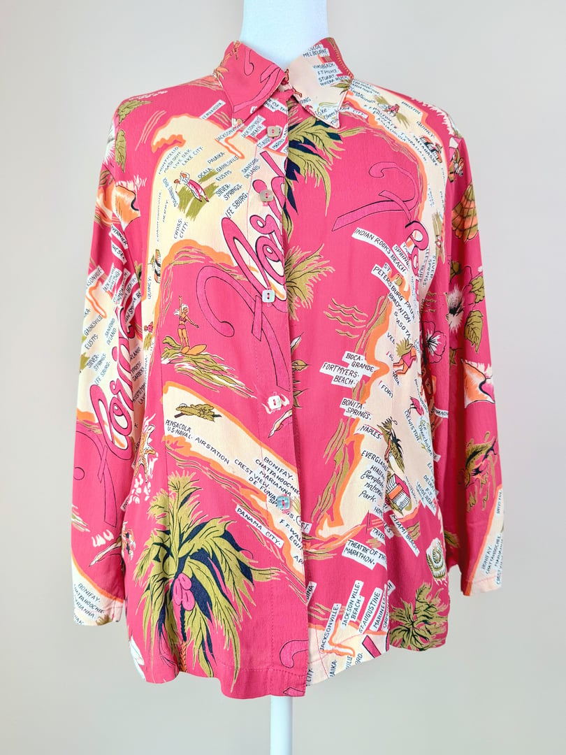 1970s women's white top featuring a vibrant pink tropical print with palm trees and text elements.