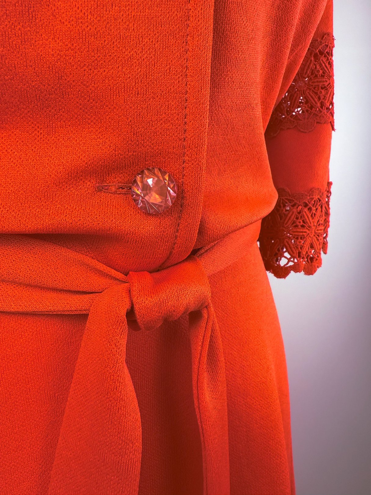 A close-up of a red lace bell dress featuring a decorative button and a tied waist detail.