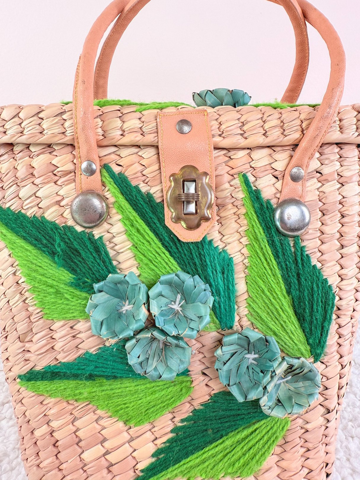 A 1970s women's straw handbag with blue floral embellishments and green leaf accents.