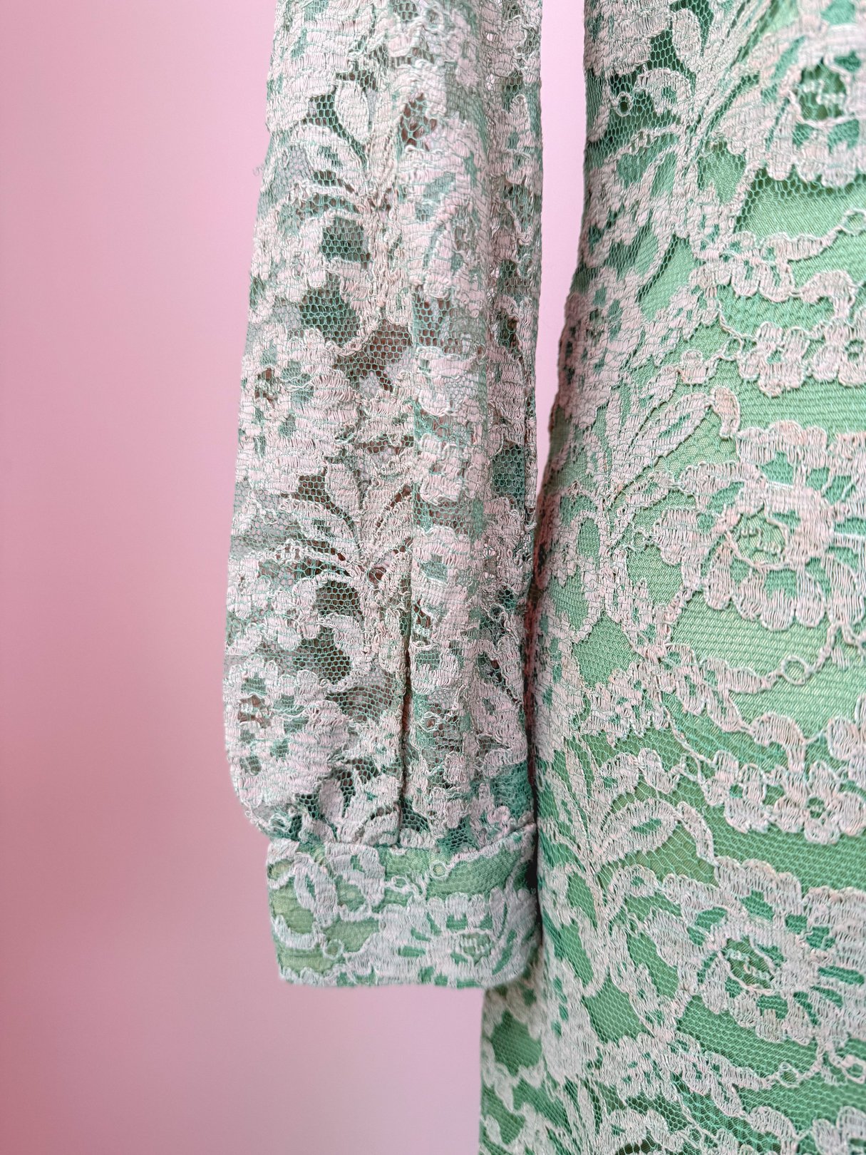 A close-up of a seafoam green 1960s women's dress featuring intricate lace detailing on the sleeve.