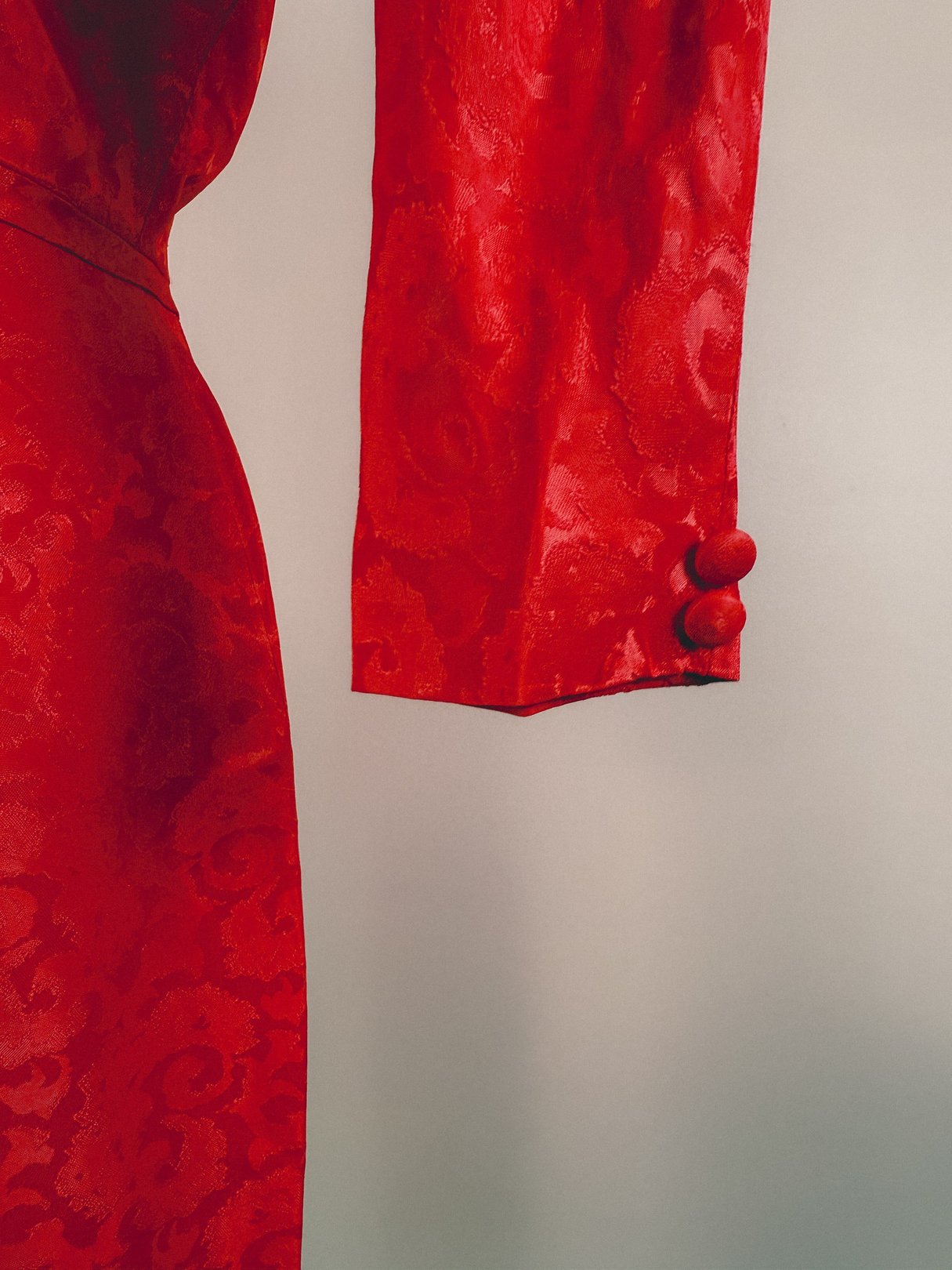 A close-up of a red damask dress featuring long sleeves with a button detail, indicative of 1950s women's fashion.