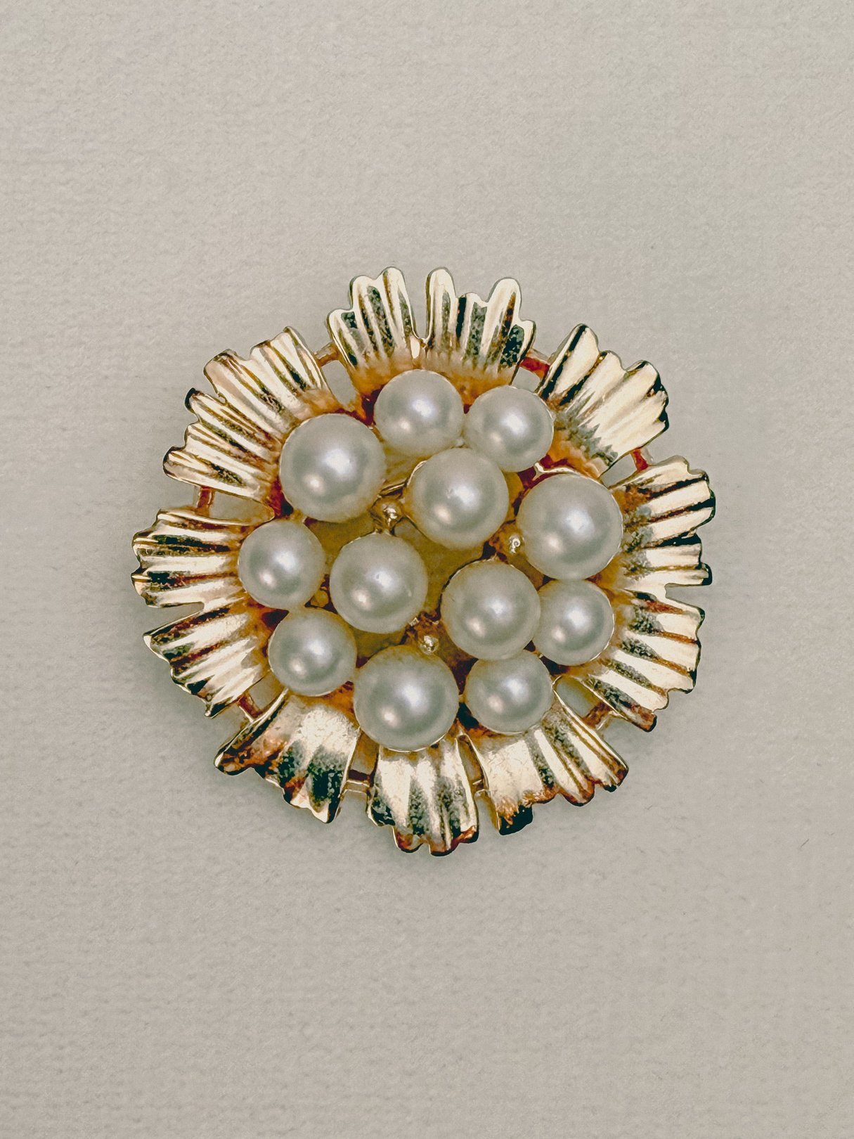 Gold-toned floral brooch featuring clusters of cream pearls, designed as costume jewelry from the 1970s for women.