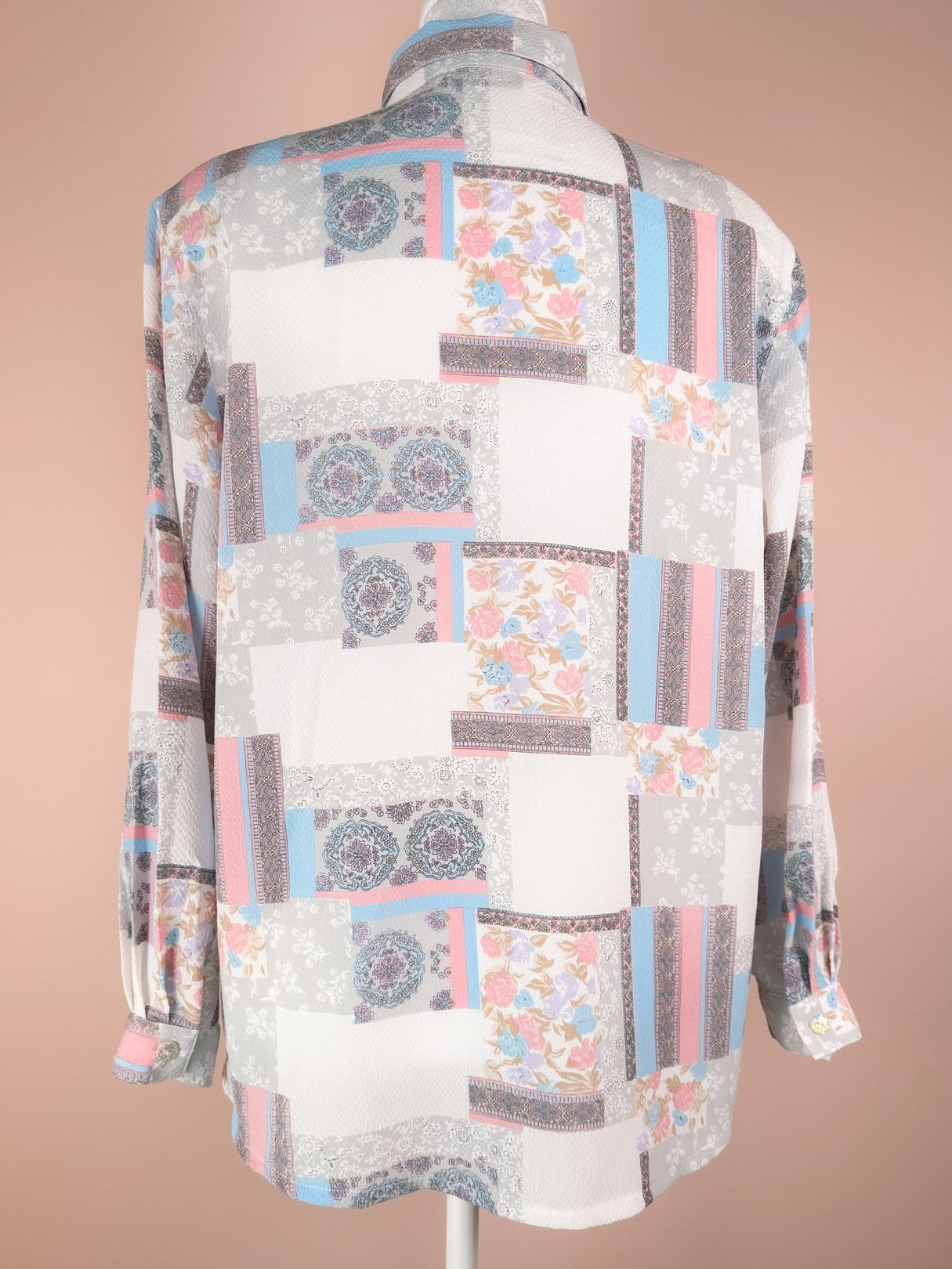 A white 1980s women's blouse featuring a colorful patchwork design with floral and geometric patterns on the back.