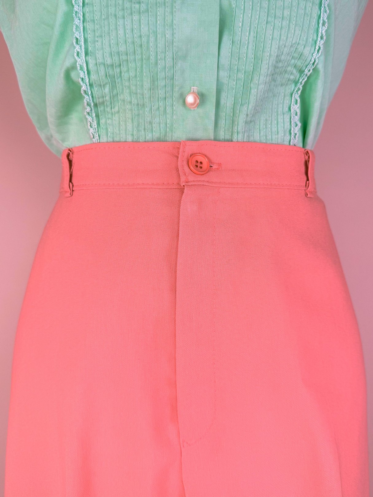 Coral pink high-waisted pants with a button closure, styled with a mint green top.