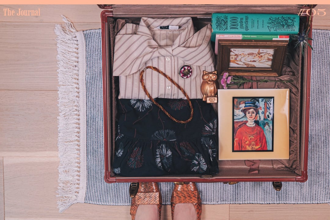 A well-organized suitcase featuring a striped shirt, floral skirt, decorative owl figurine, books, a framed artwork, and stylish shoes.