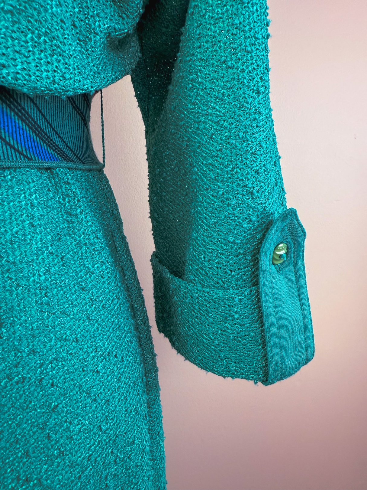 Teal 1980s women's dress featuring a textured fabric and button detail on the sleeve.