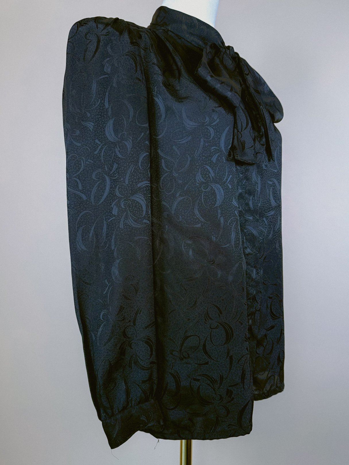 Black 1980s women's top featuring a bow detail at the neckline and a patterned black fabric.