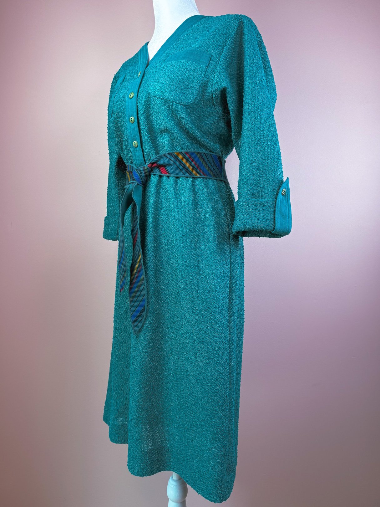 Teal 1980s dress featuring a v-neck, front button closure, and a colorful striped belt.