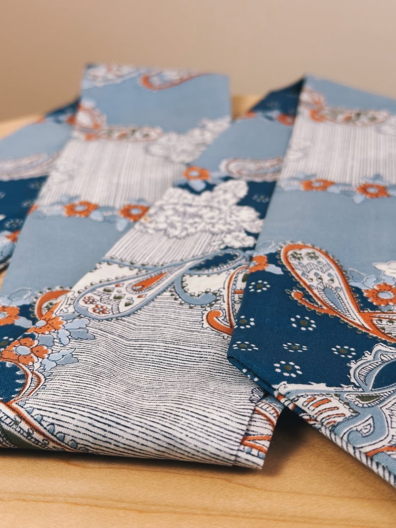 Light blue paisley scarf with floral and ornamental patterns, reflecting a 1970s style, suitable for women.