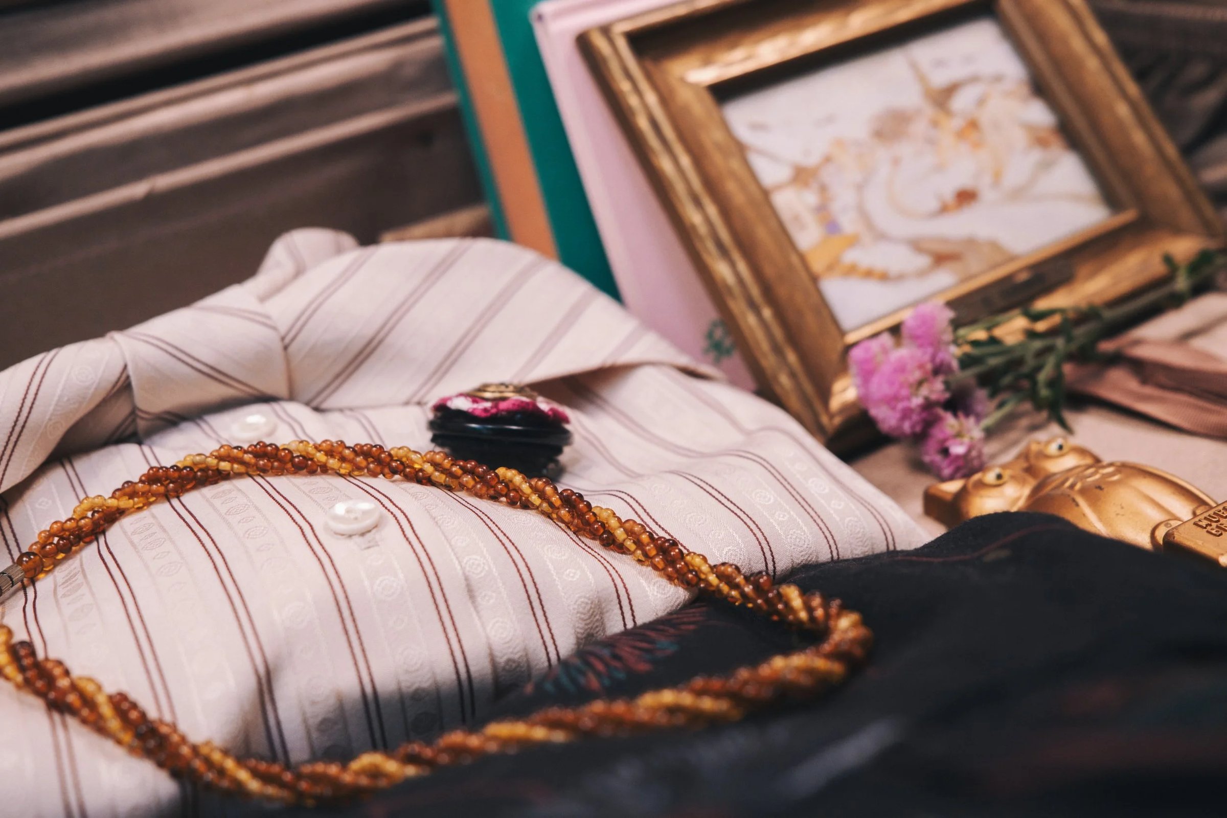 A vintage shirt with button details, a decorative brooch, a beaded necklace, and a framed art piece displayed among flowers and a small figurine.