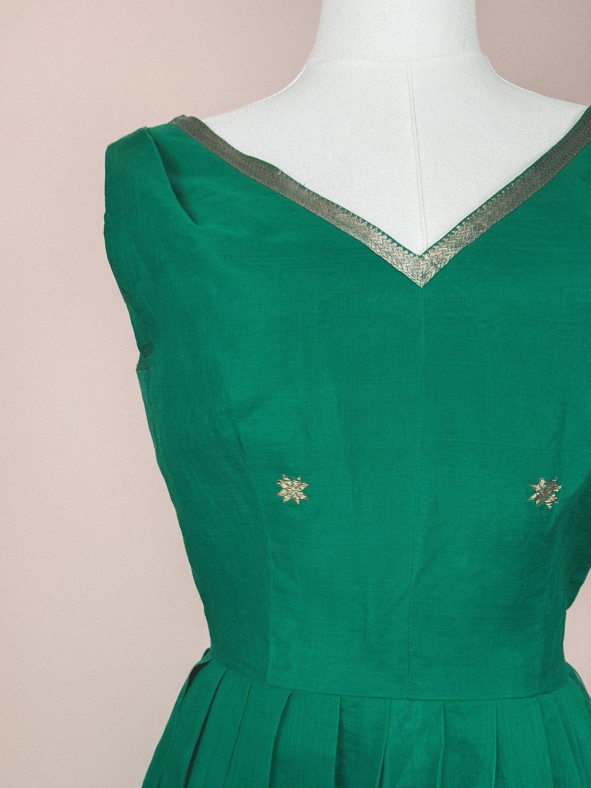 Green 1950s women's dress with a V-neckline and gold starburst embellishments on the bodice.