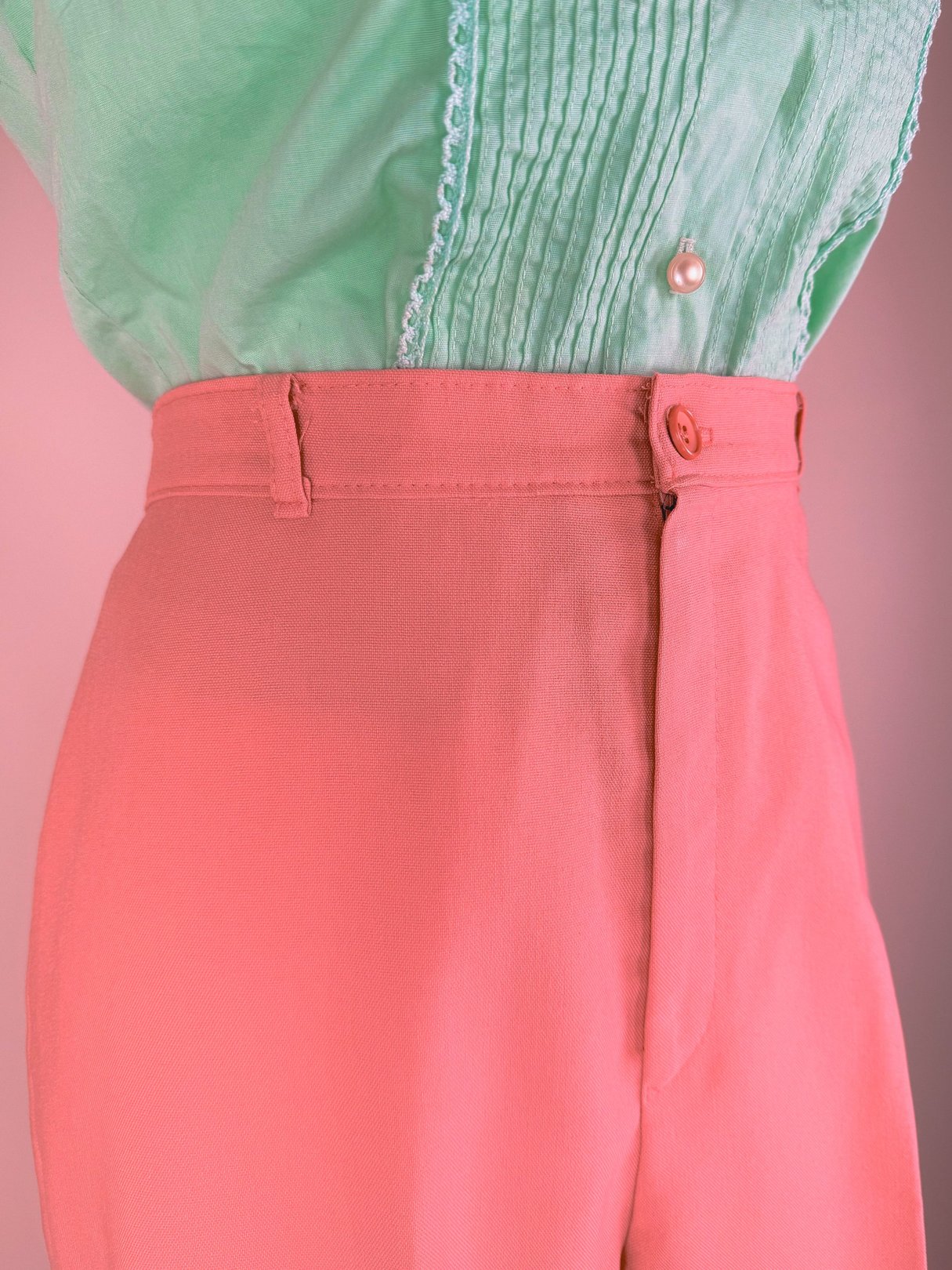 Coral pink 1970s women's pants with a high waist and button closure detail.