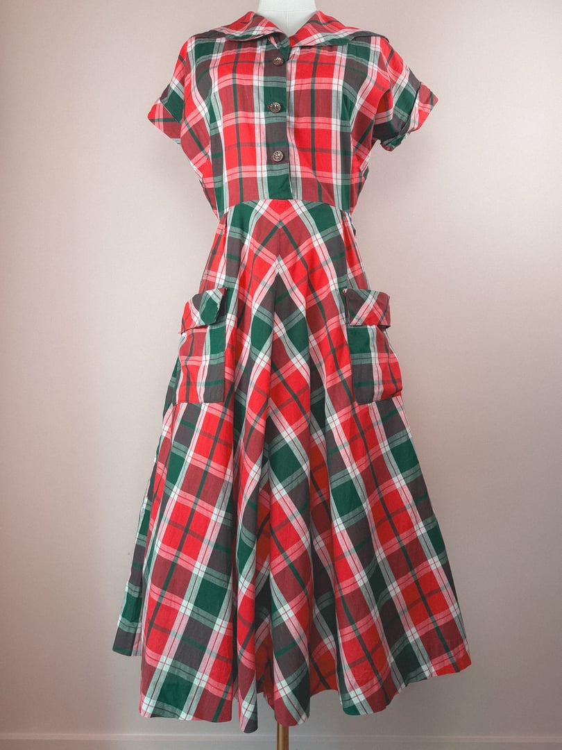Red and green plaid dress with short sleeves and side pockets, styled in a 1950s silhouette for women.