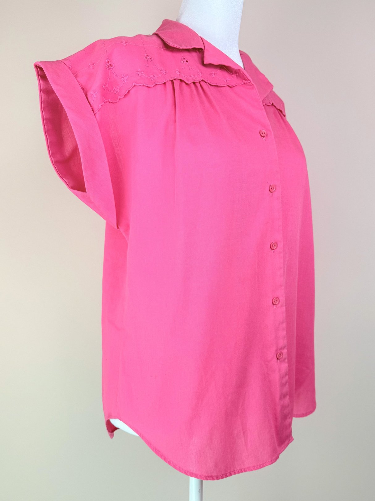 A women's pink blouse from the 1980s featuring a button-down front and short sleeves with a textured yoke.