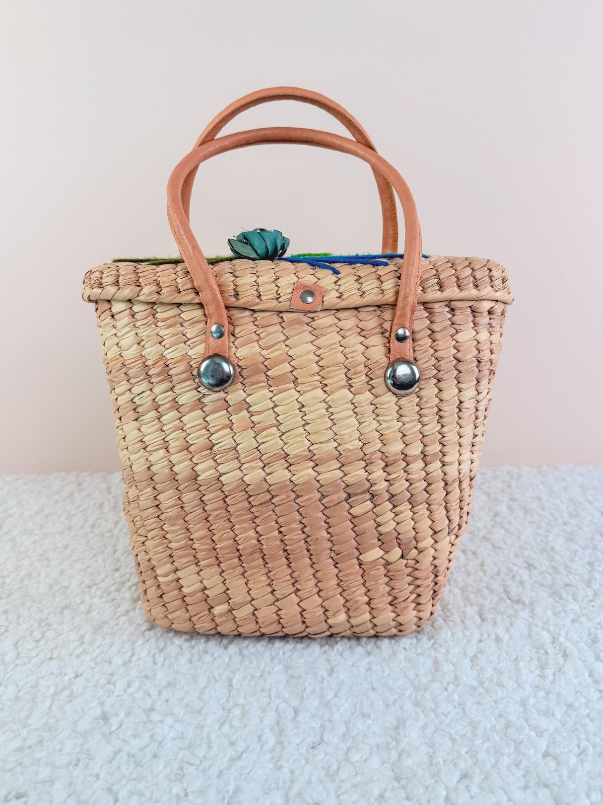 Woven straw handbag with leather handles, featuring a blue interior, styled in a 1970s design for women.